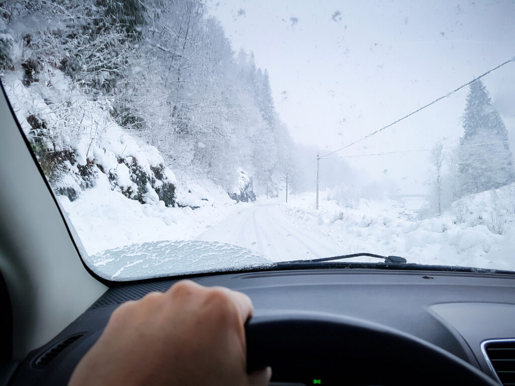 DE closeup of man driving on a snowing road through window. Wintercamping.