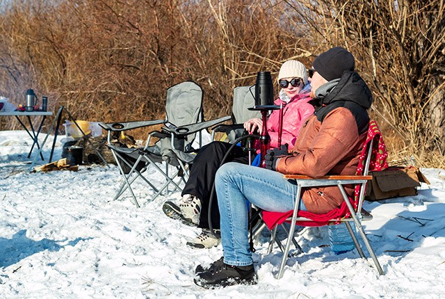 DE couple sitting on lawn chairs in the snow. Wintercamping