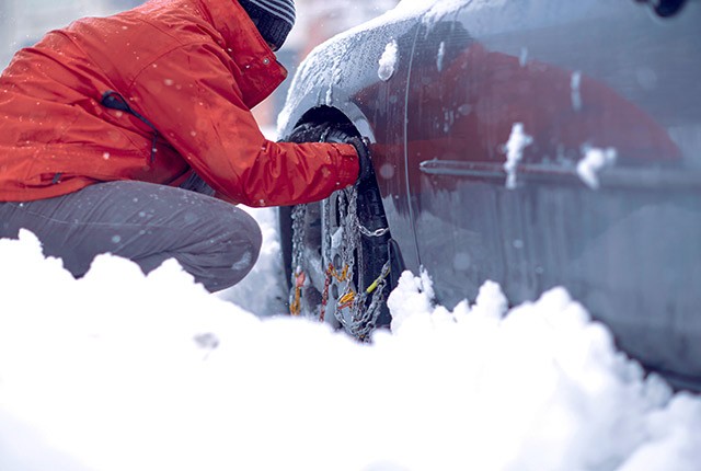 Man in red jacket putting chains on car tires in the snow.